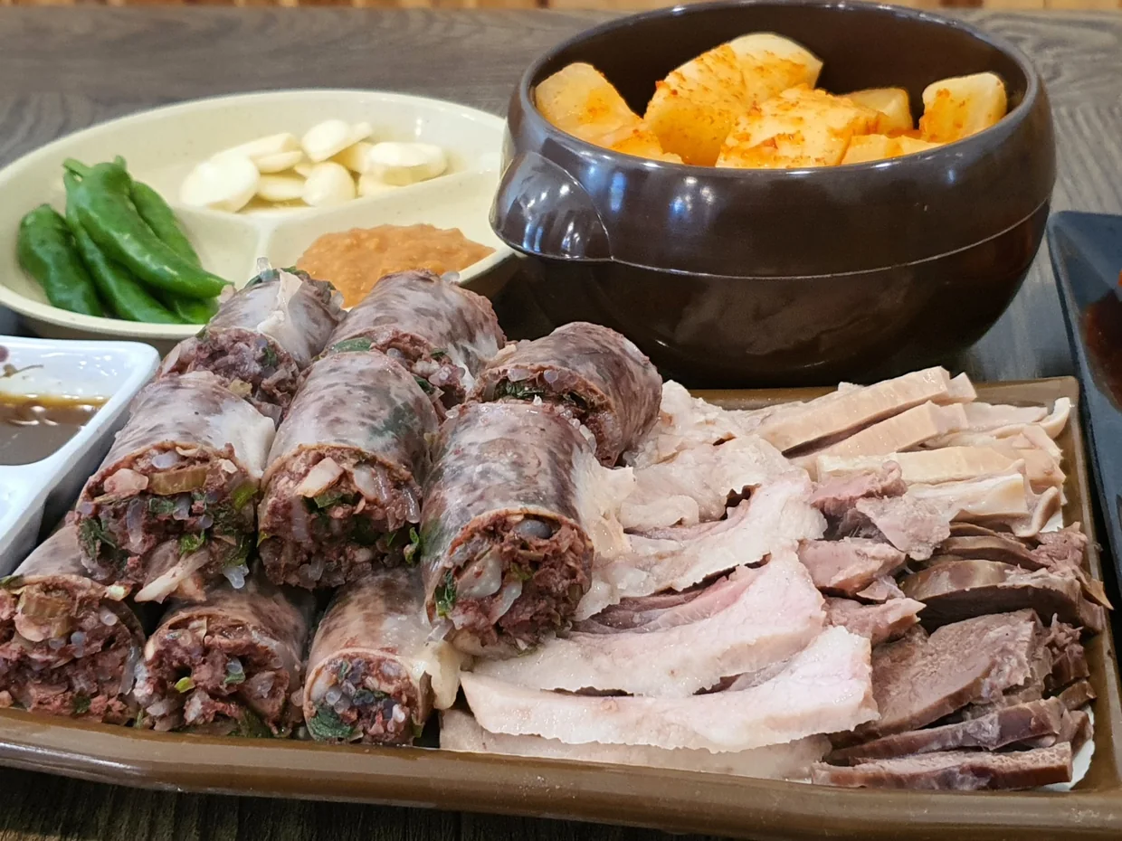 순대와 삶은 고기를 함께 담은 접시 — 깍두기 단지, 고추·마늘·쌈장